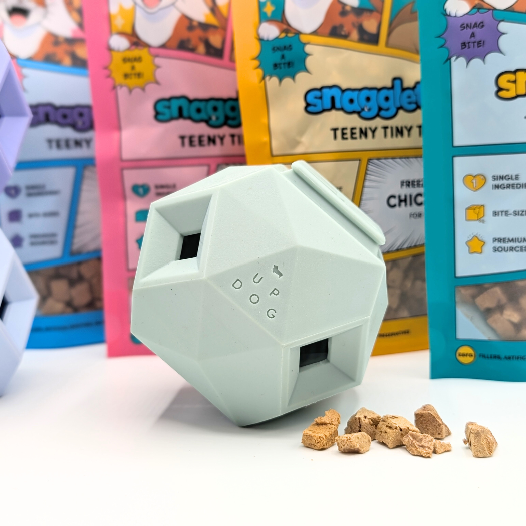 The Odin Dog puzzle toy with treats in front of Snagglepuss cat food packages
